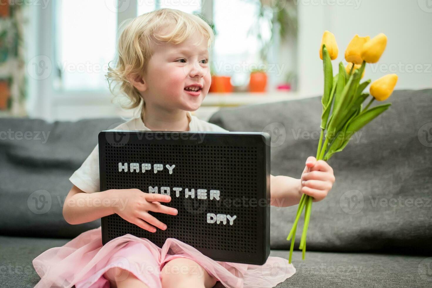 liten flicka innehar en bukett av gul tulpaner och en tecken den där säger Lycklig mors dag. barn ger blommor till mor för Semester. foto