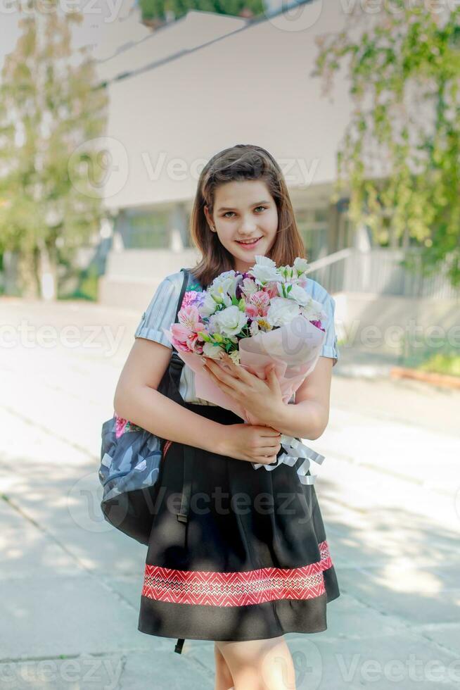 tonåring flicka innehar en bukett av blommor och går till skola. studerande gratulerar med kvinnors dag på Mars 8 lärare. högtider på skola. födelsedag på barn av 11 år. foto