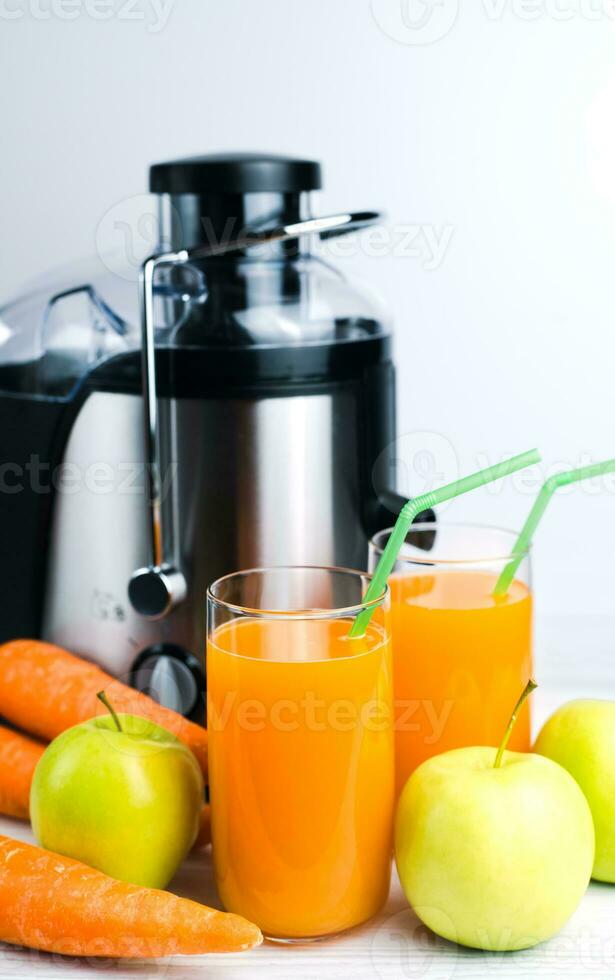 en glas av multivitamin juice, äpplen, morötter och en juicepress på de tabell. naturlig och friska juicer. vertikal Foto. närbild. foto