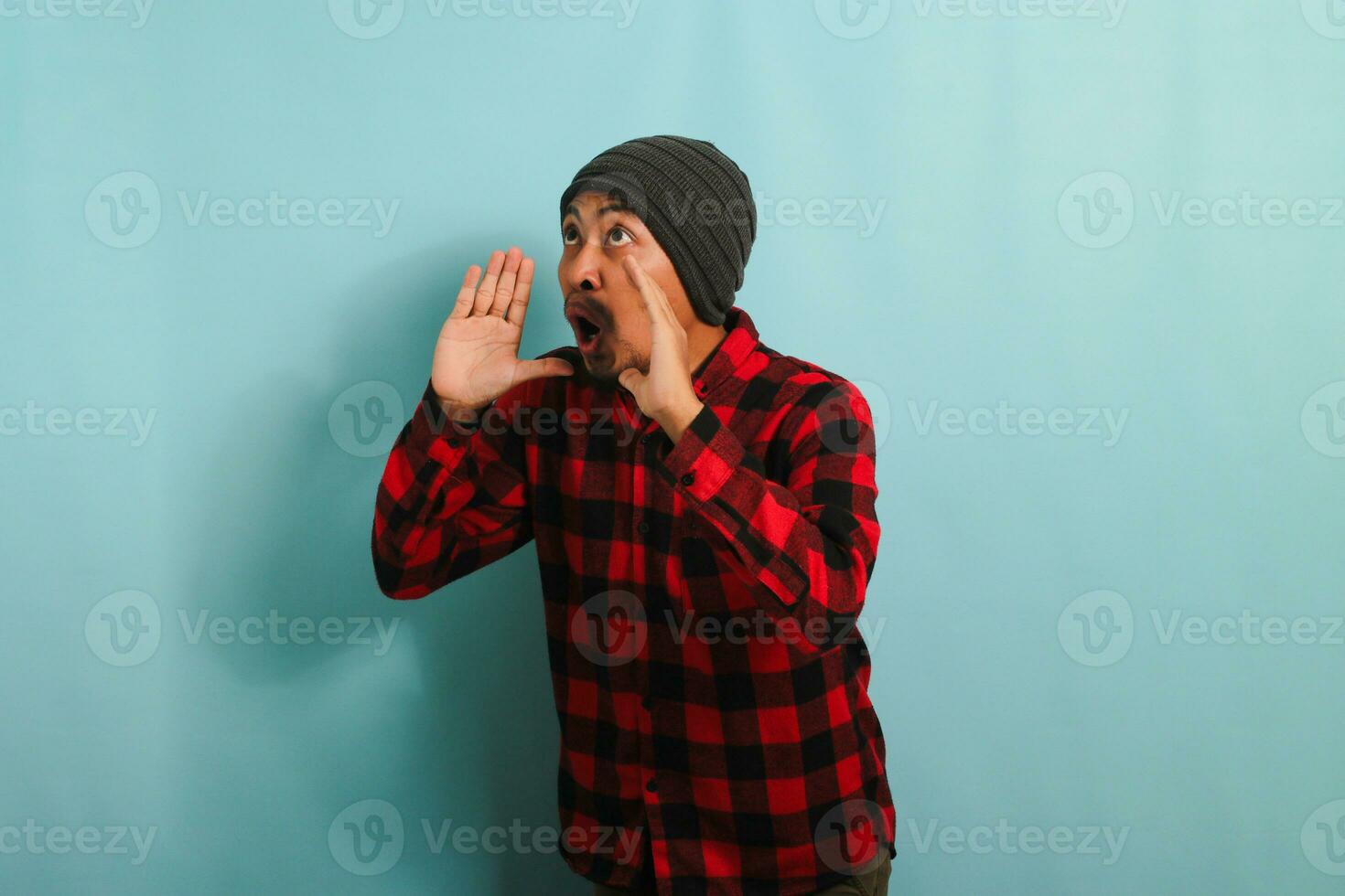 upphetsad ung asiatisk man skrikande talande Bra Nyheter, isolerat på en blå bakgrund foto