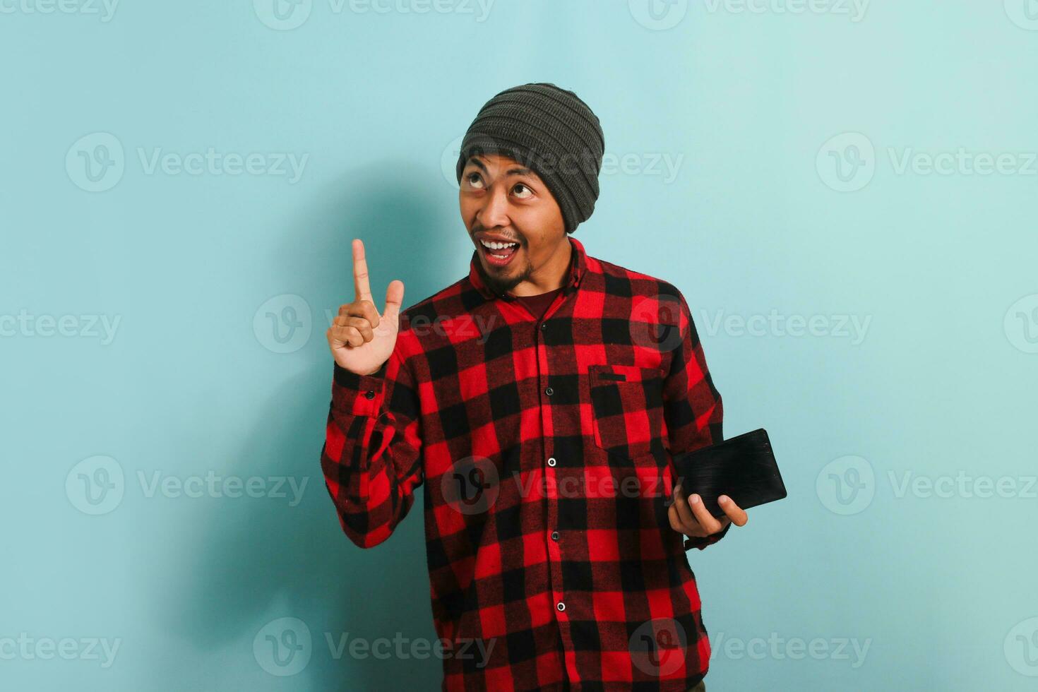 upphetsad ung asiatisk man pekande åt sidan på kopia Plats medan innehav plånbok, isolerat på blå bakgrund foto