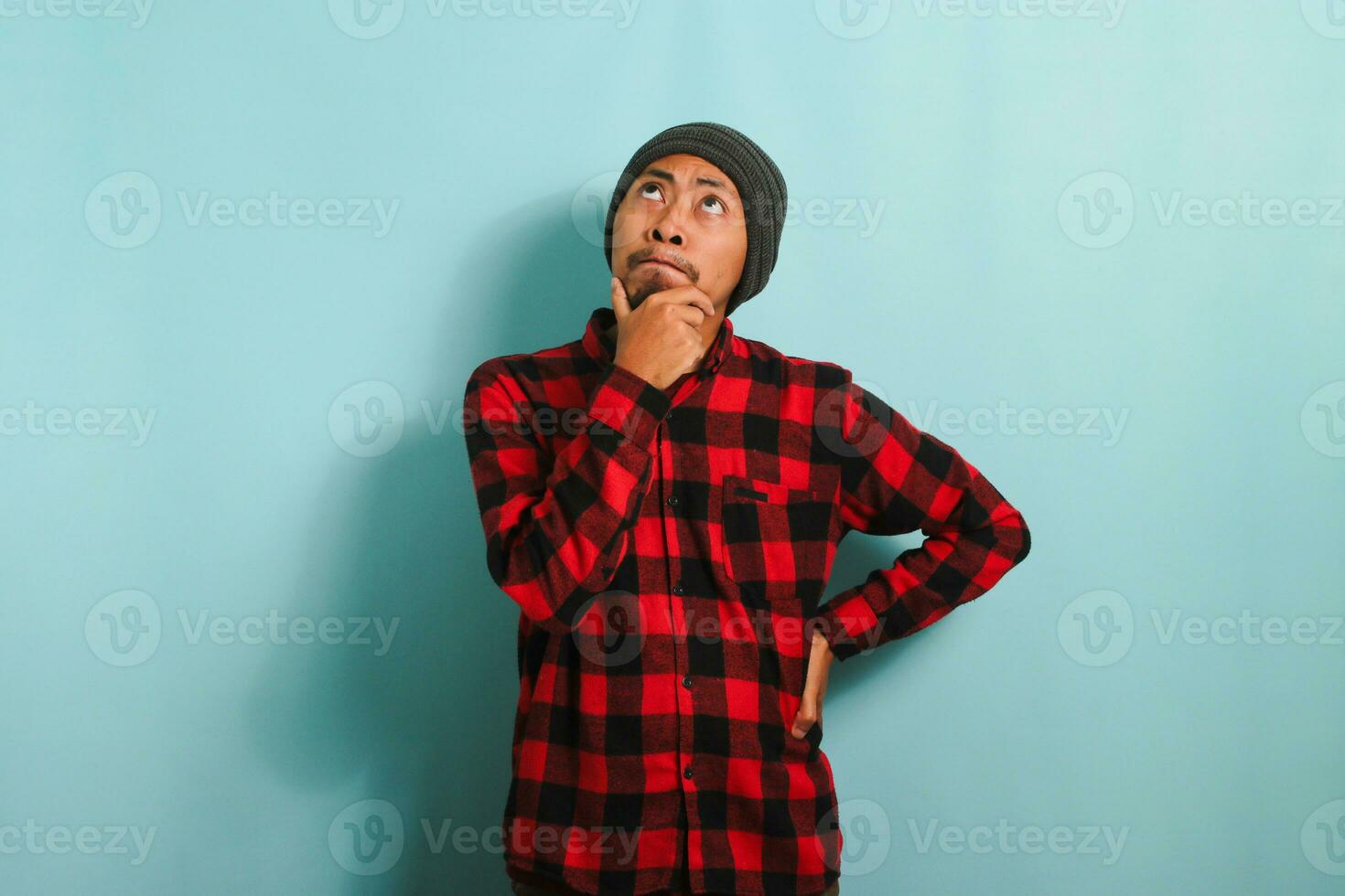 omtänksam ung asiatisk man innehar hans haka, framställning planer, isolerat på en blå bakgrund foto
