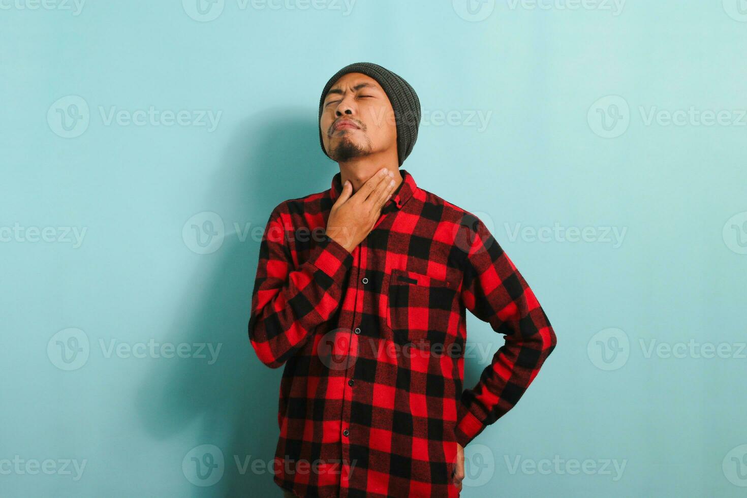 sjuk ung asiatisk man innehav hans nacke, lidande från en öm hals, isolerat på blå bakgrund foto