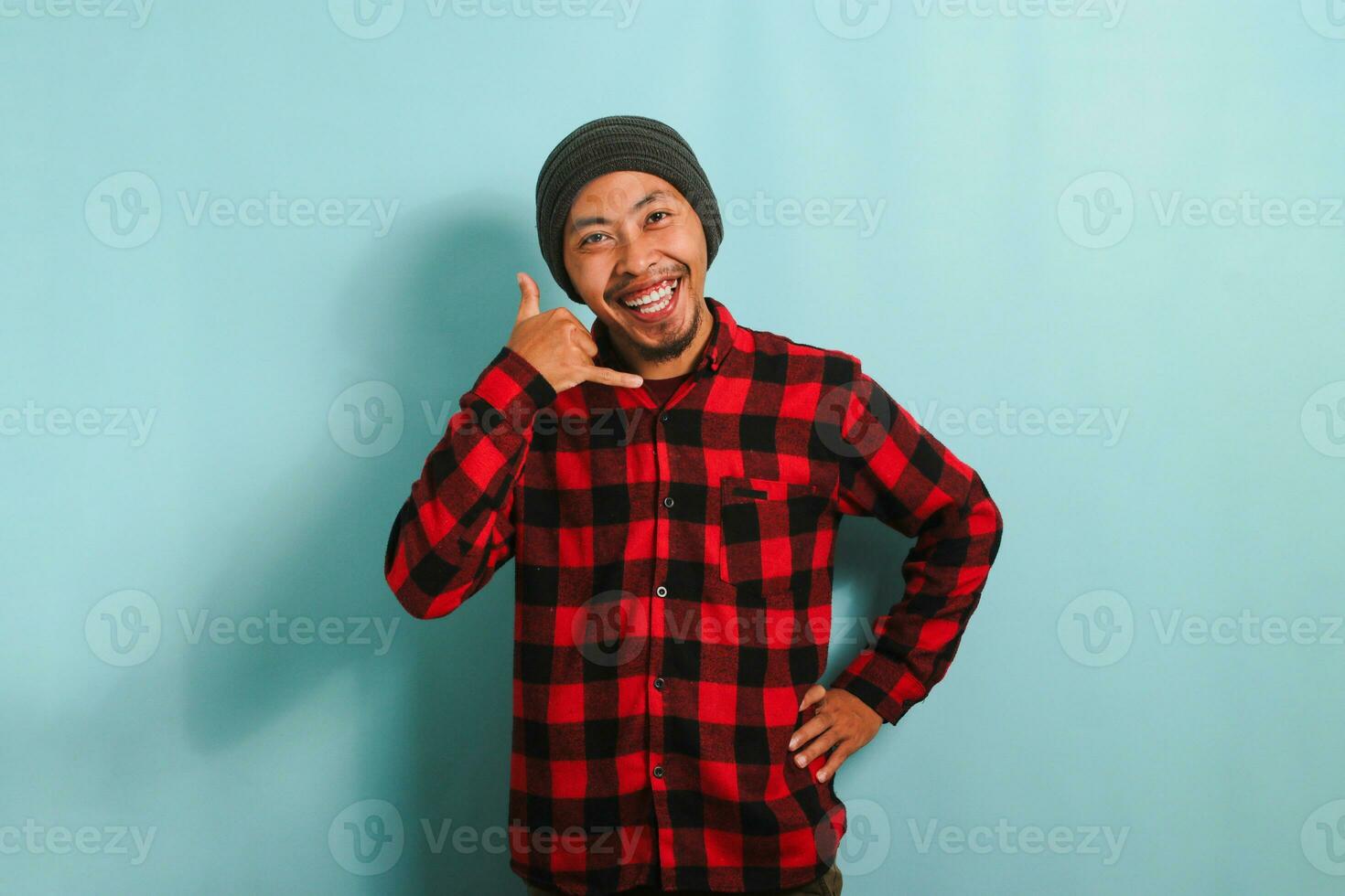 ett upphetsad ung asiatisk man bär en mössa hatt och en röd pläd flanell skjorta gör en ring upp mig gest med hans hand, isolerat på en blå bakgrund foto