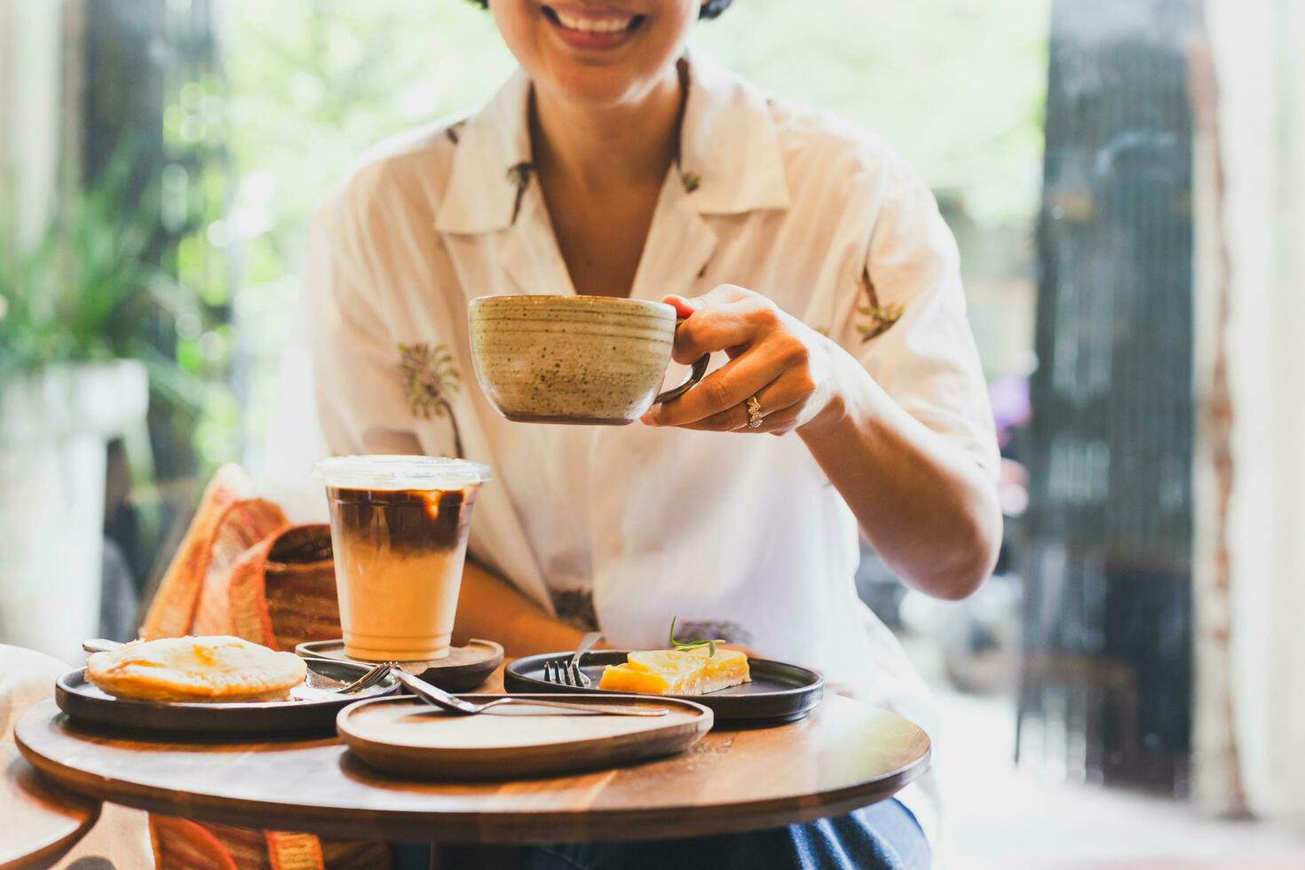 Lycklig kvinna drycker kaffe och äter kaka i Kafé. foto