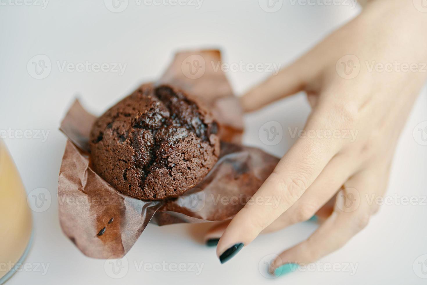 kvinnans hand plockar upp chokladmuffin från bordet foto