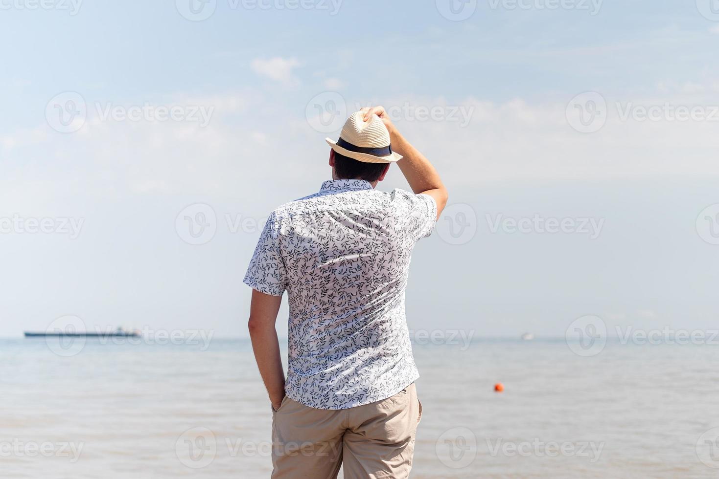 ung man i sommarkläder som står på en pir, havet i bakgrunden foto