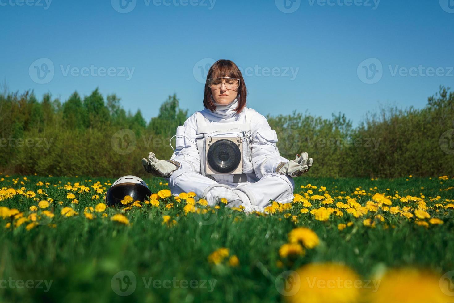 kvinna astronaut utan hjälm sitter på en grön gräsmatta bland blommor foto
