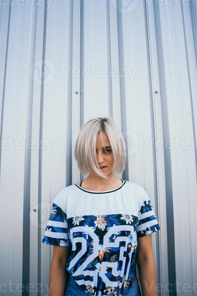 kvinna med kort vitt hår står på bakgrunden av metallvägg foto