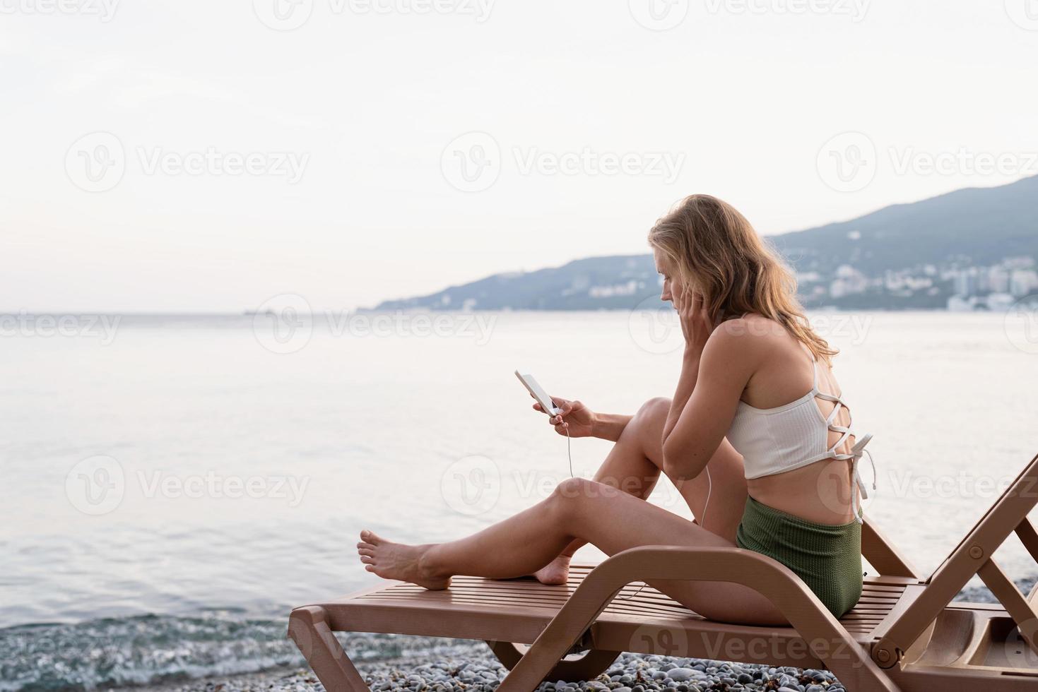 ung kvinna som sitter på solstolen och lyssnar på musiken foto