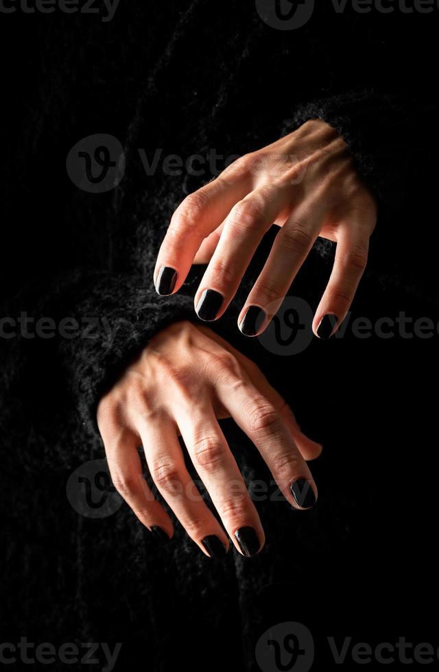 läskiga kvinna halloween händer med svarta naglar på mörk bakgrund foto