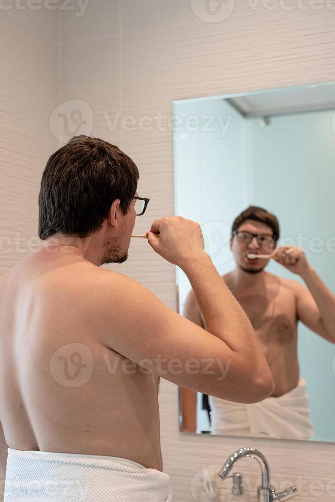 en ung man borstar tänderna i badrummet foto