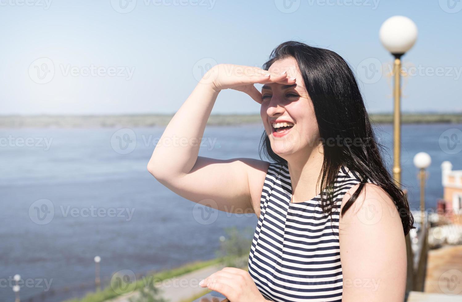 ung skrattande kvinna som står vid floden och njuter av utsikten foto