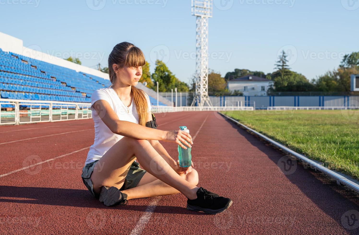 tonåring flicka sitter på stadion spår med vila dricksvatten foto