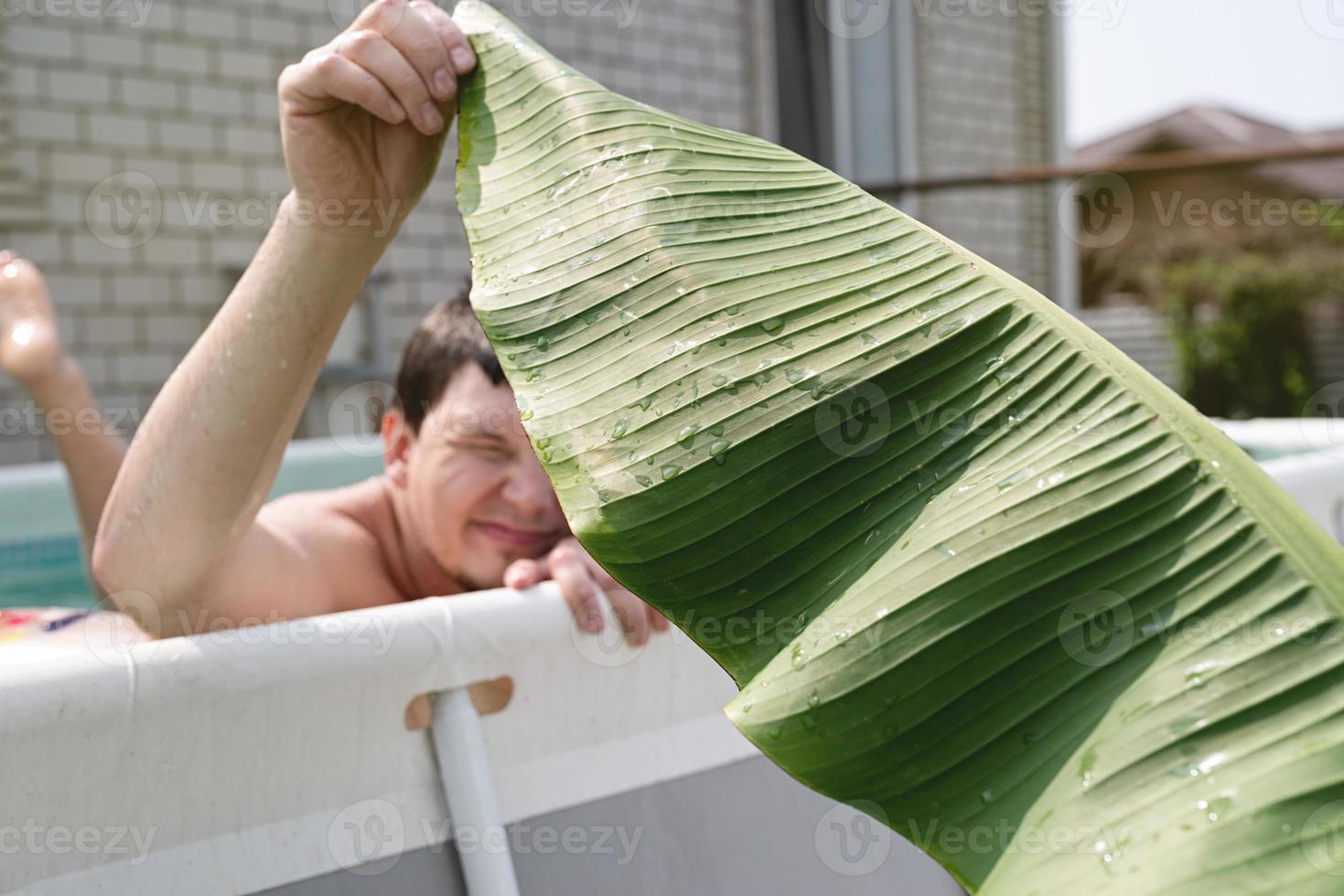 ung man som simmar i poolen och håller ett palmblad foto