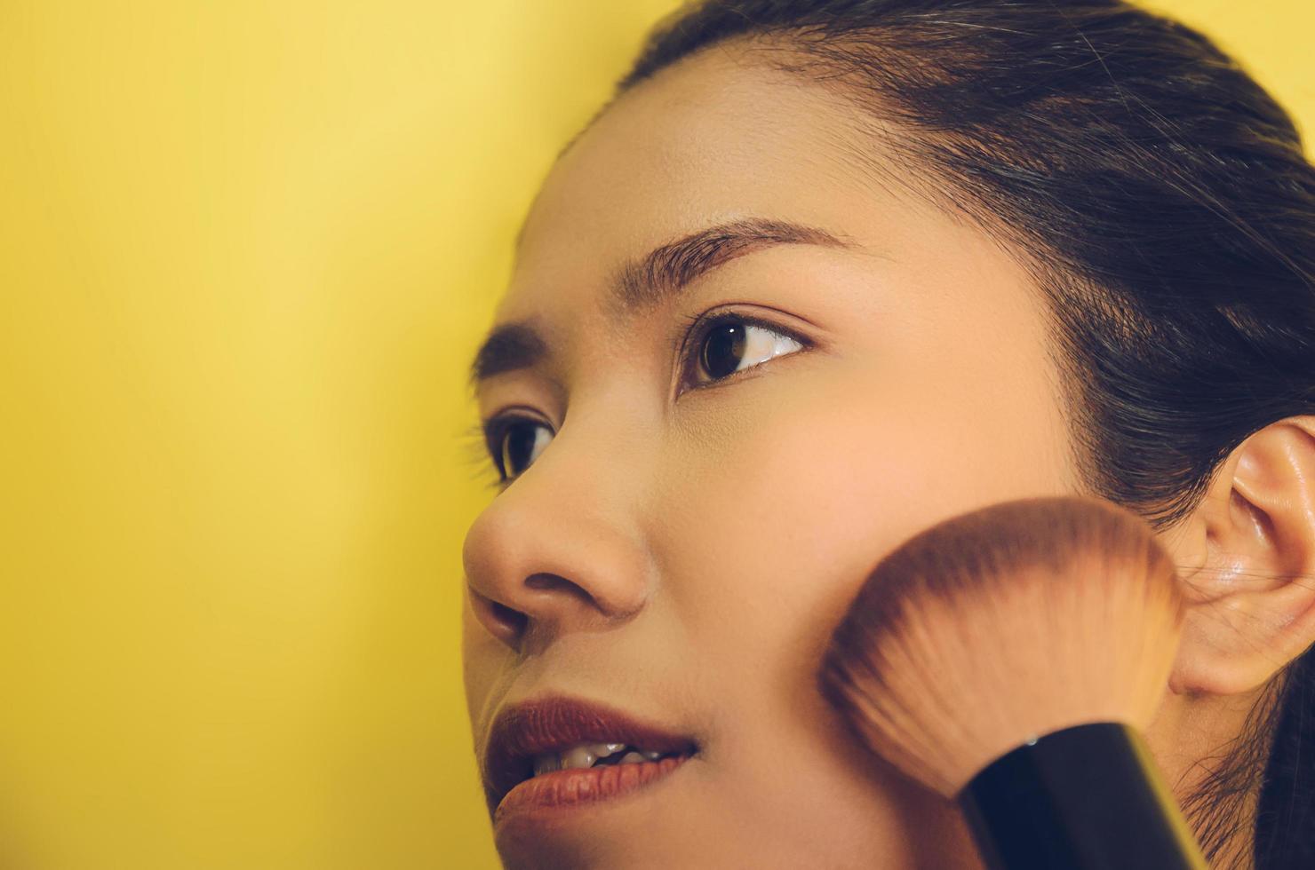 skönhet ansikte av asiatisk kvinna genom att applicera borstar på huden med kosmetika. foto