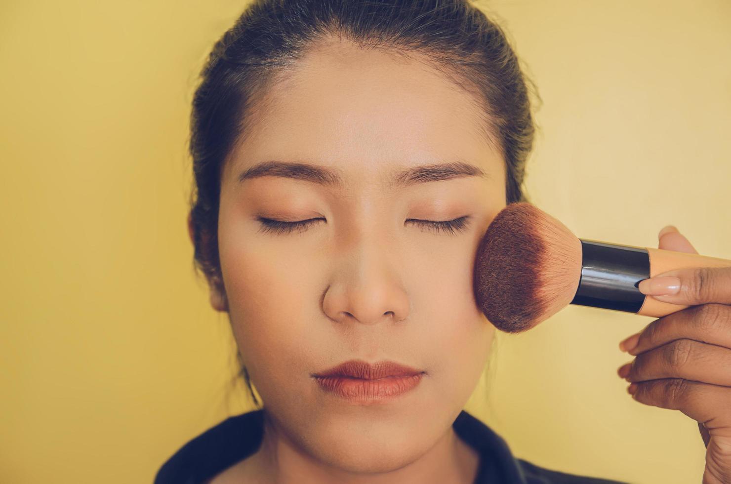 skönhet ansikte av asiatisk kvinna genom att applicera borstar på huden med kosmetika. foto