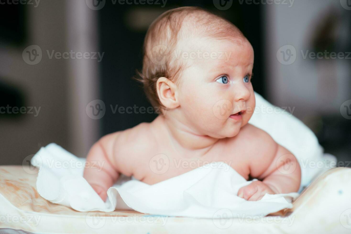 Lycklig bebis flicka lögner på en vit ark i henne rum foto