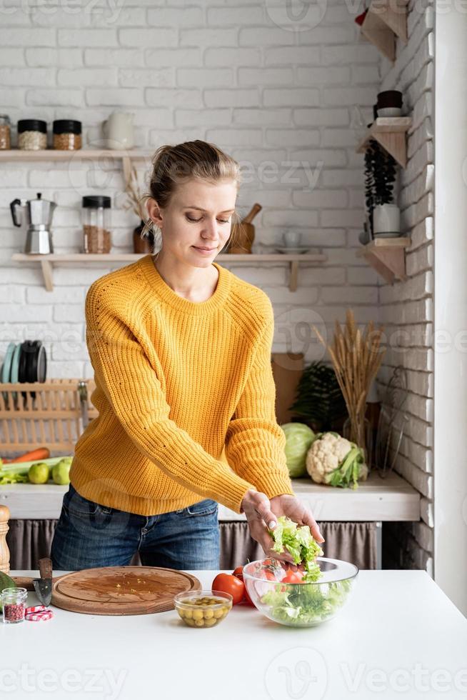 ung vacker kvinna som förbereder grekisk sallad i köket som skär sallad foto