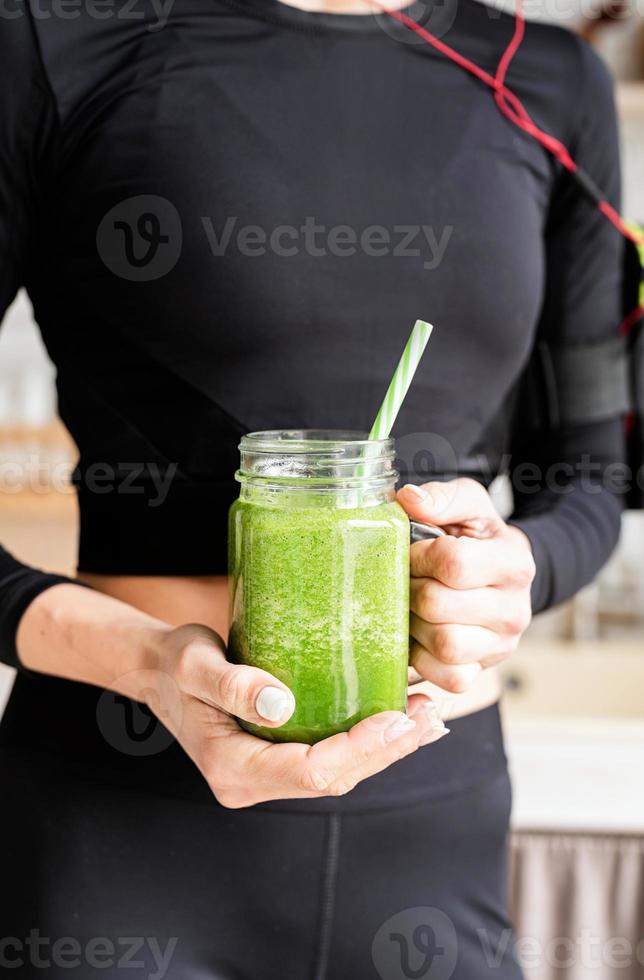 kvinna i svarta sportkläder som håller en burk grön smoothie foto