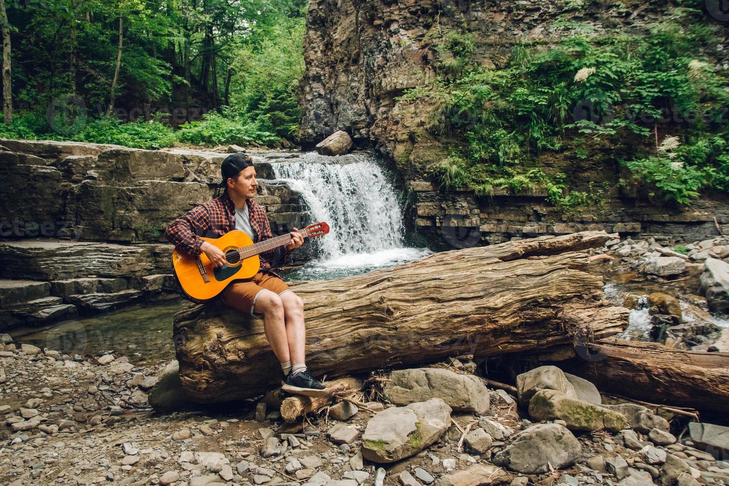 man spelar gitarr som sitter vid ett vattenfall foto