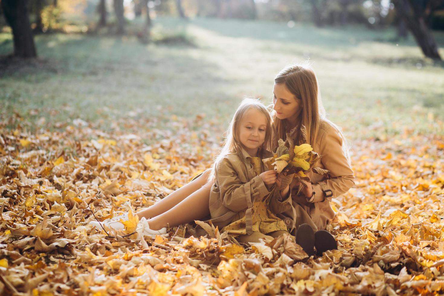 mamma och hennes dotter sitter och har kul i höstparken. foto