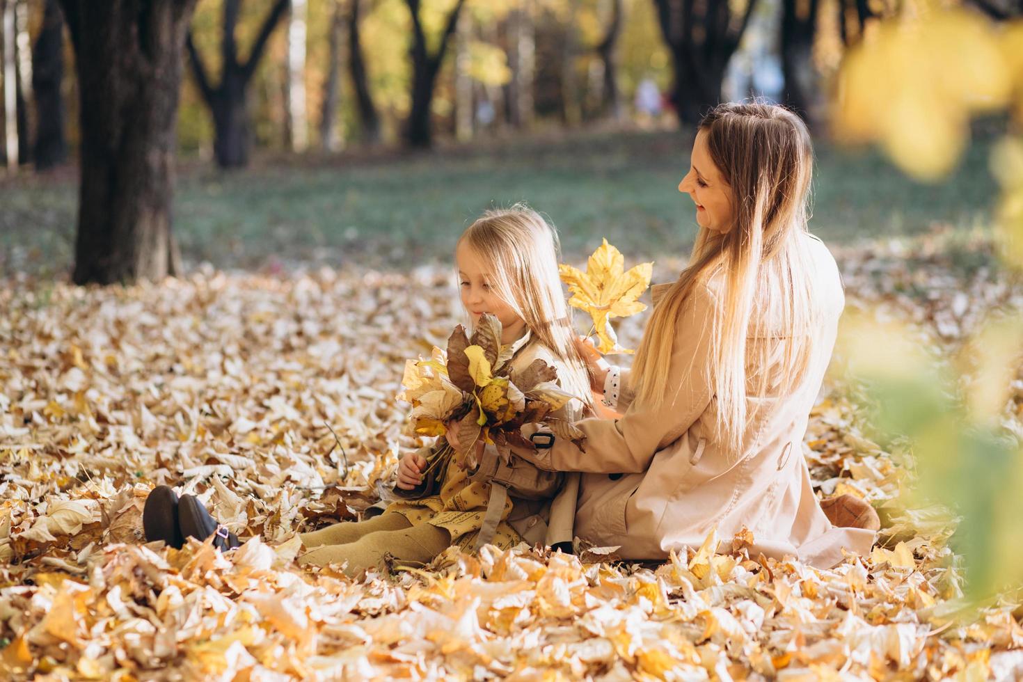 mamma och hennes dotter sitter och har kul i höstparken. foto