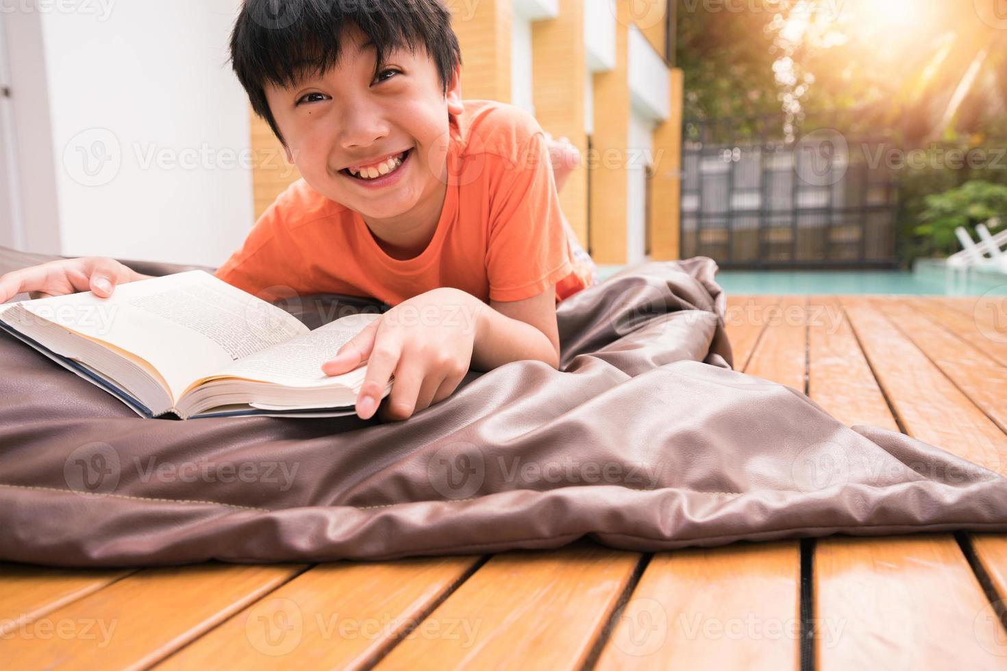 en pojke som ler med en bok på träbord. lära hemma foto