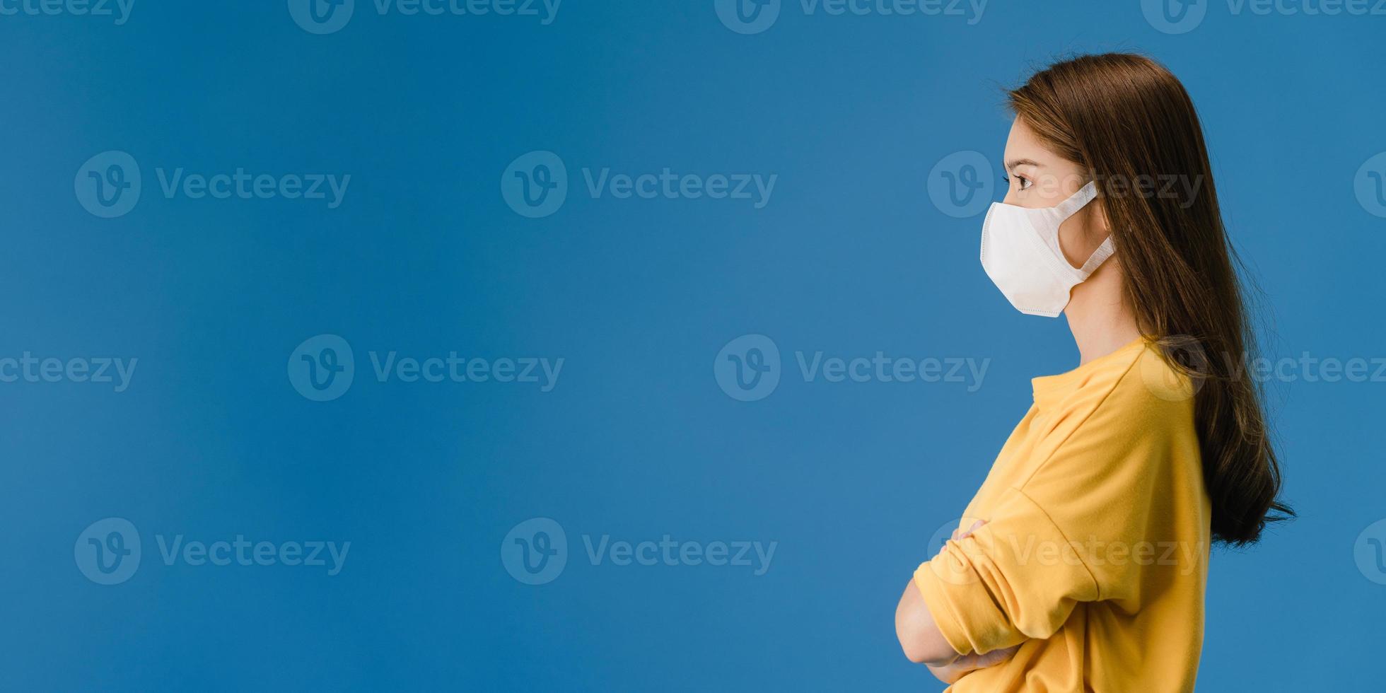 ung asiatisk tjej bär ansiktsmask titta på tomt utrymme på blå bakgrund. foto