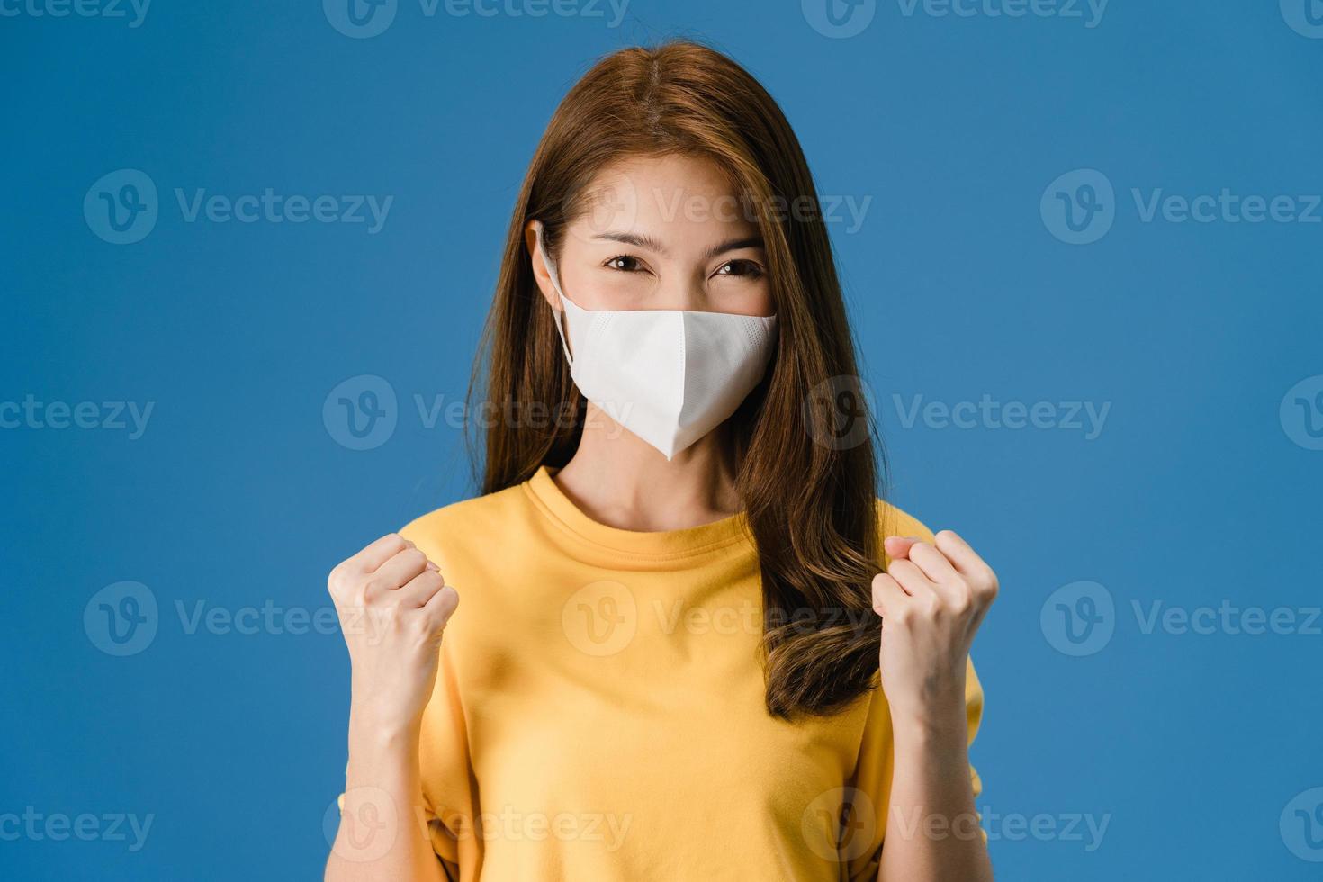 ung asiatisk tjej bär ansiktsmask som visar fredstecken på blå bakgrund. foto