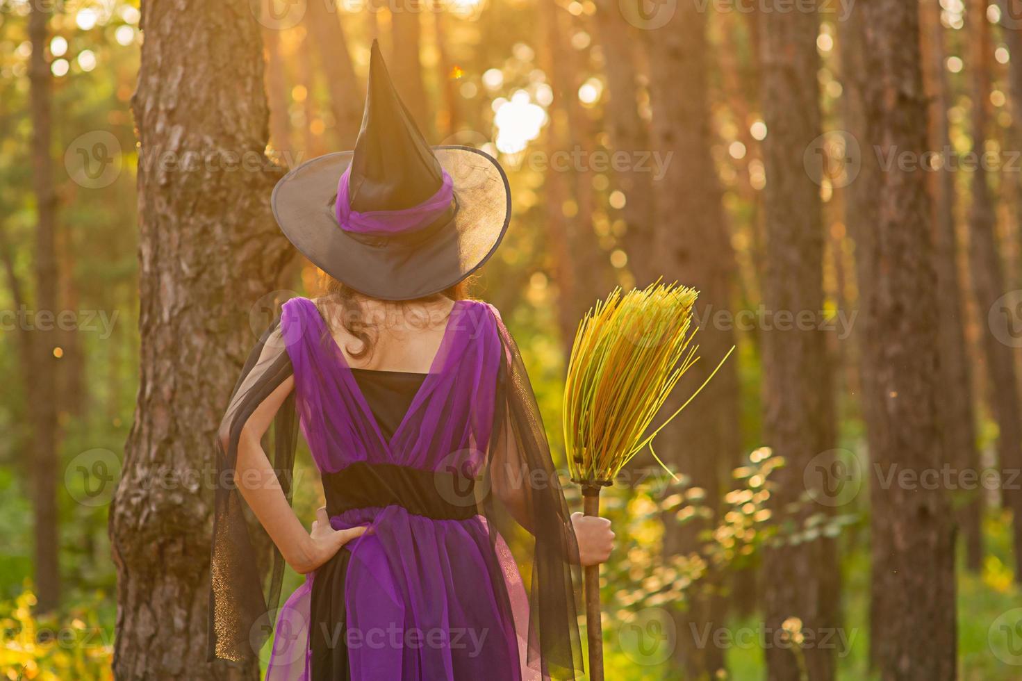 ung flicka i en halloweenkostym i skogen med en kvast foto