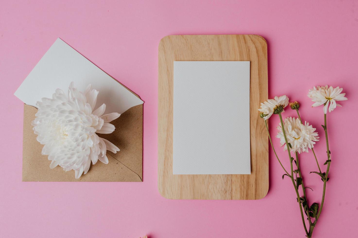 brunt kuvert, blomma och tomt kort på träplatta med rosa foto