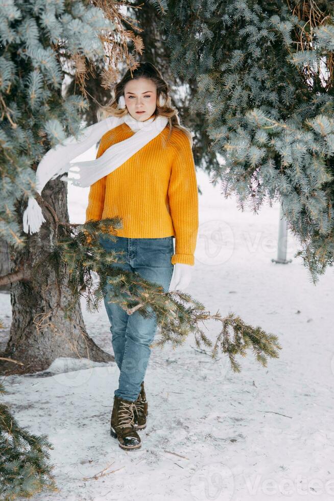 tonåring blond i en gul Tröja utanför i vinter. en Tonårs flicka på en promenad i vinter- kläder i en snöig skog foto