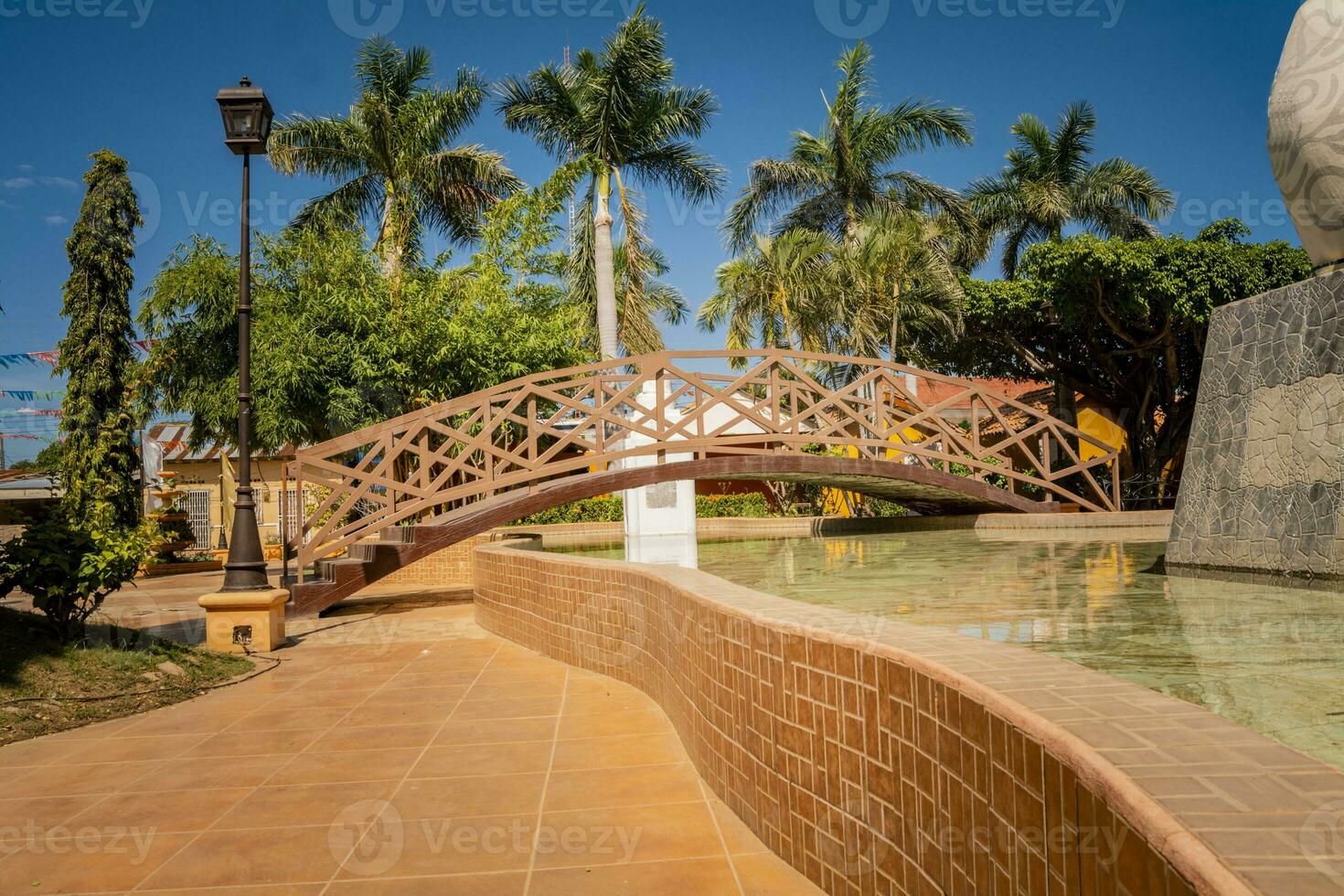 nagarote central parkera. se av en trevlig och avslappnad parkera med en vatten fontän. traditionell, sida se av en små trä- bro över en vatten fontän i en lugna parkera. parkera av nagarote, nicaragua foto