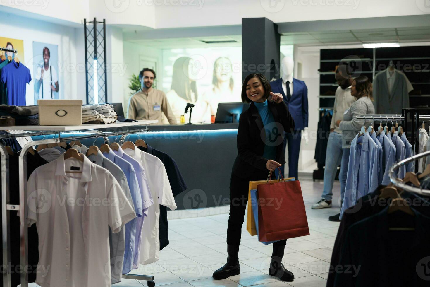 Lycklig kvinna shopaholic dans med handla påsar efter framställning framgångsrik inköp i Kläder Lagra. glad kund innehav papper paket med kläder och rör på sig kropp till musik i köpcenter foto