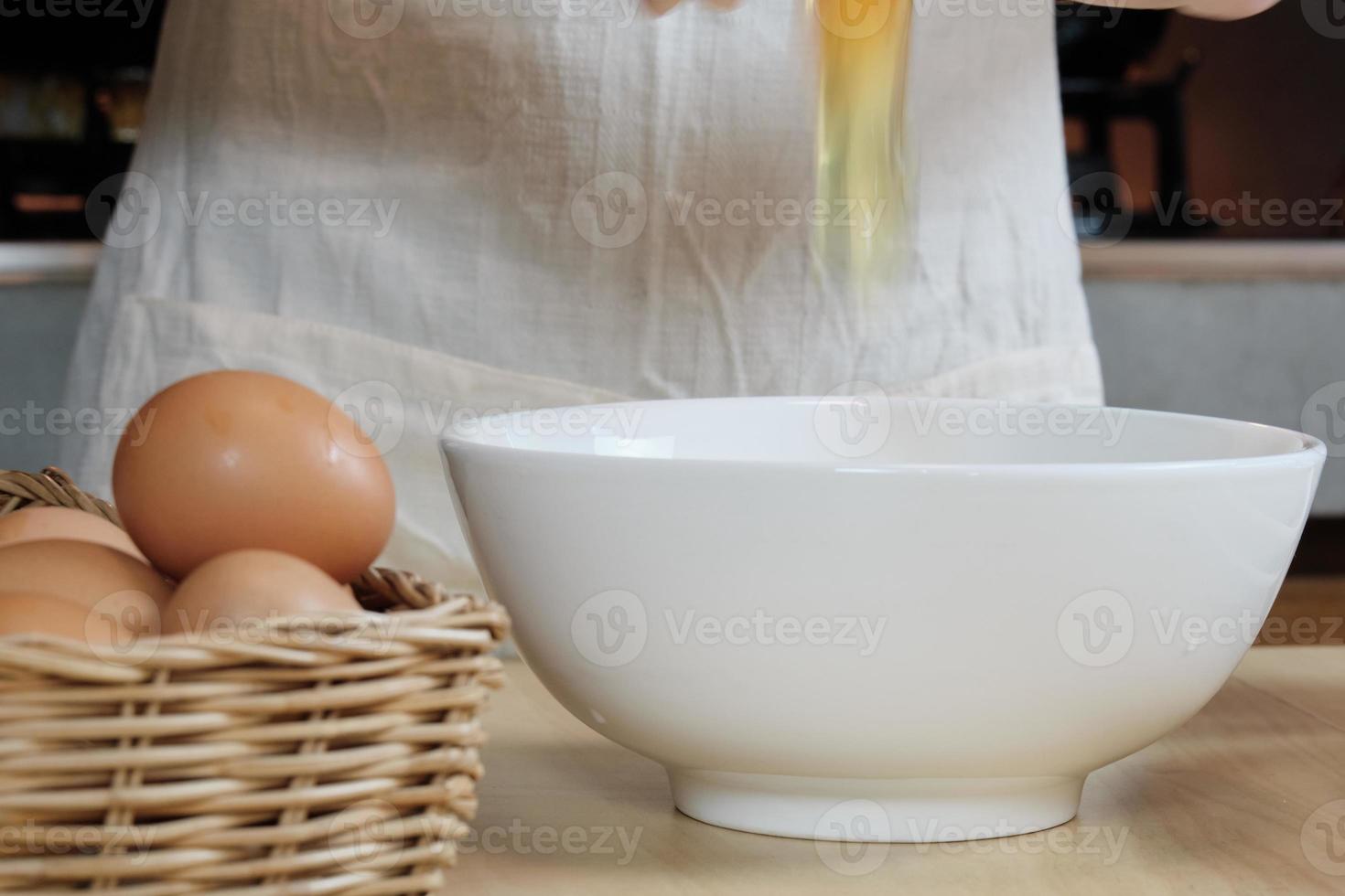 kvinnlig kock i ett vitt förkläde knäcker ett ägg i hemmets kök. foto