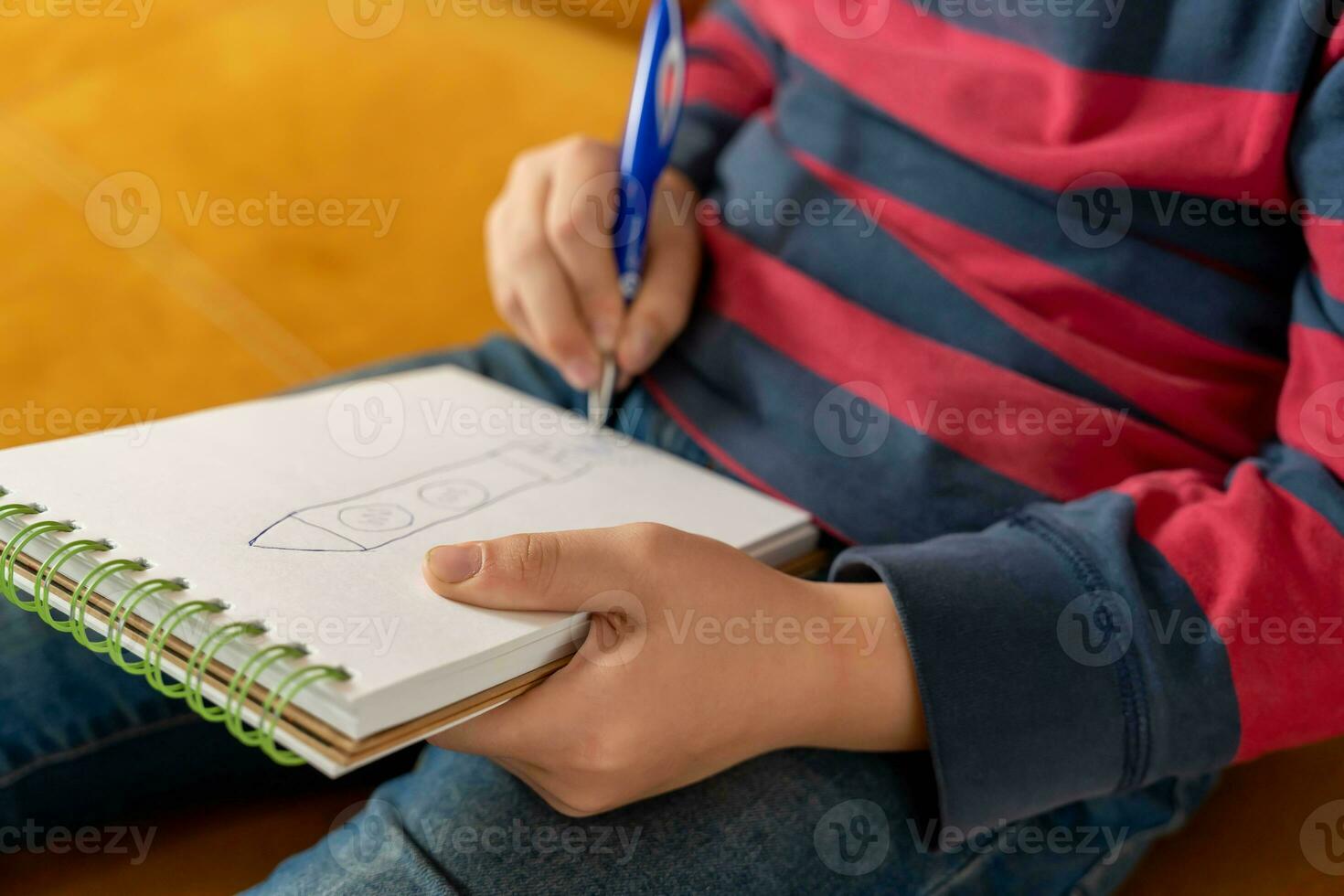 en pojke koncentrering på teckning i hans anteckningsbok. han kopplingar de penna i hans hand foto