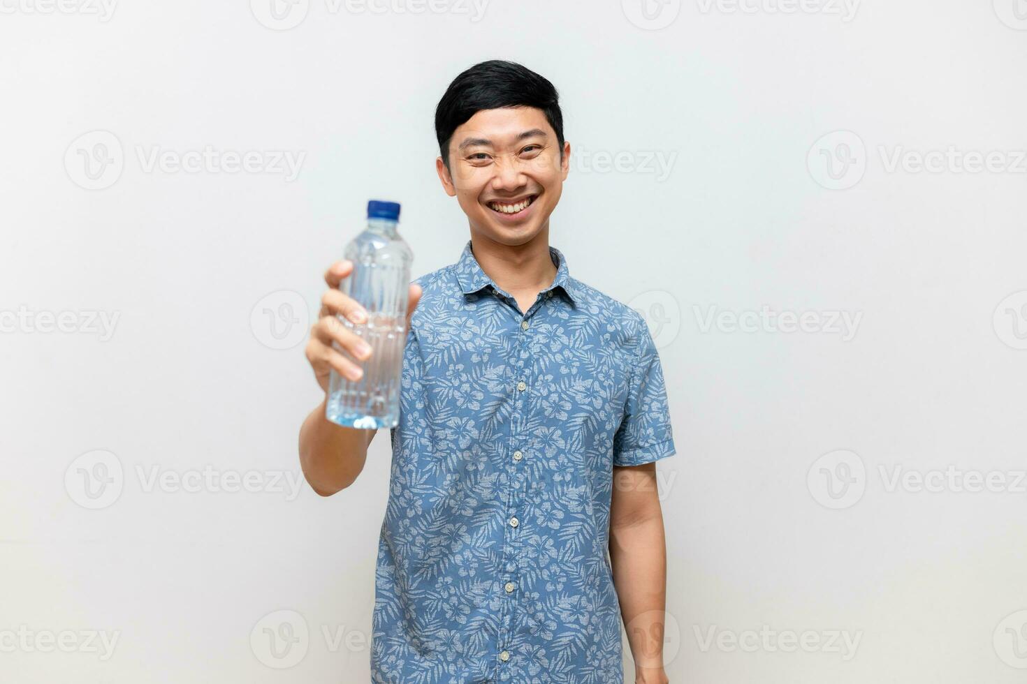 positiv asiatisk man blå skjorta håll flaska av vatten Lycklig leende isolerat foto