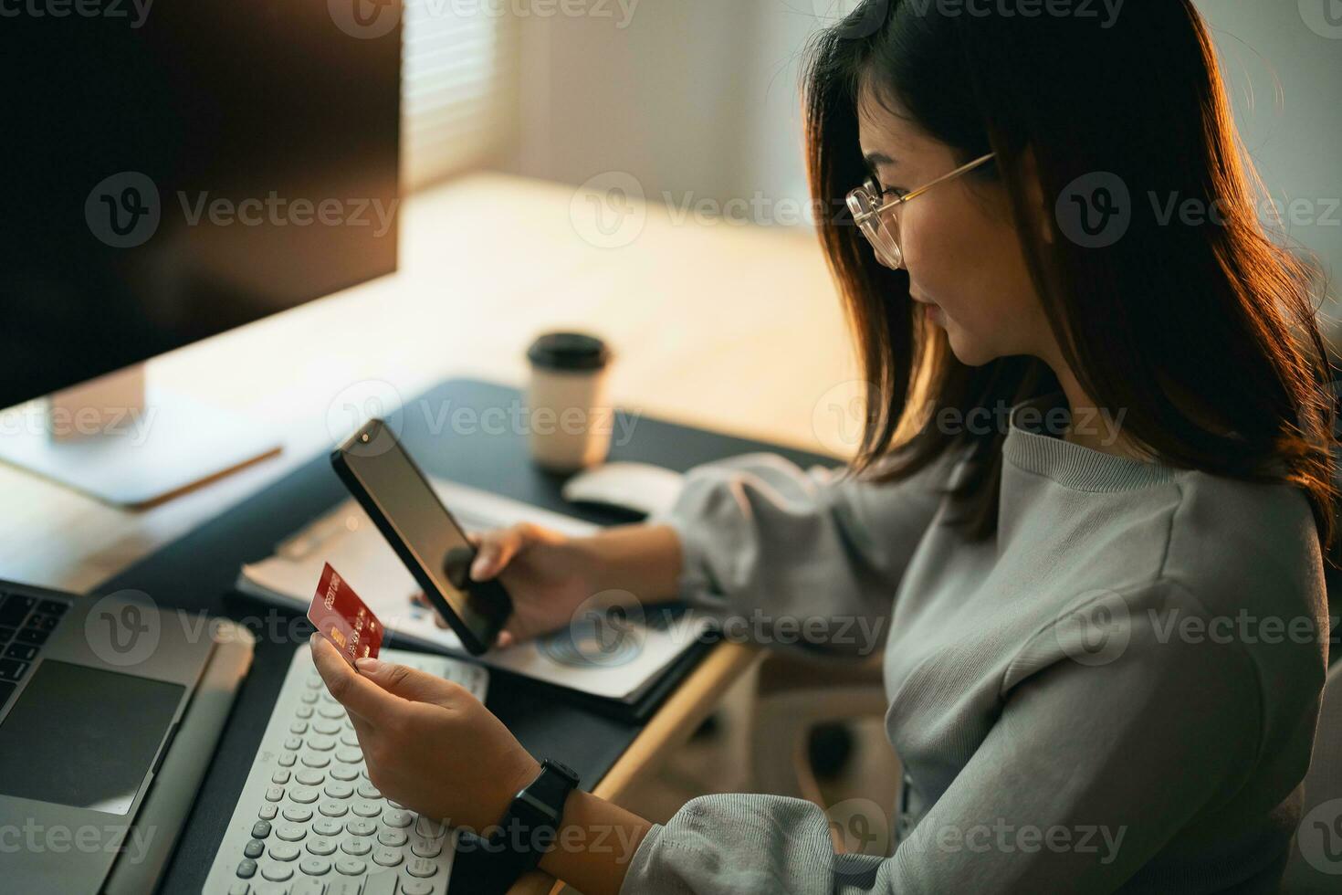 kvinna innehav kreditera kort och använder sig av mobil till handla uppkopplad. asiatisk kvinna bär glasögon arbetssätt på Hem. uppkopplad handla, e-handel, internet bank, utgifterna pengar, arbetssätt från Hem begrepp. foto