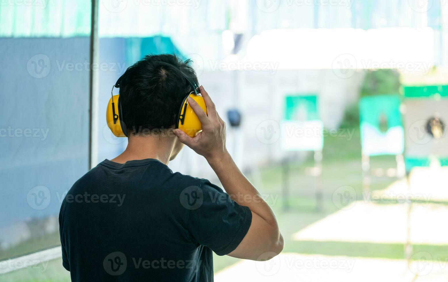 asiatisk skytten man bär ljud inställande hörlurar och svart kläder praktiserande skytte kort pistol på de skytte räckvidd. skytte sporter för meditation och självförsvar, rekreations aktiviteter. foto