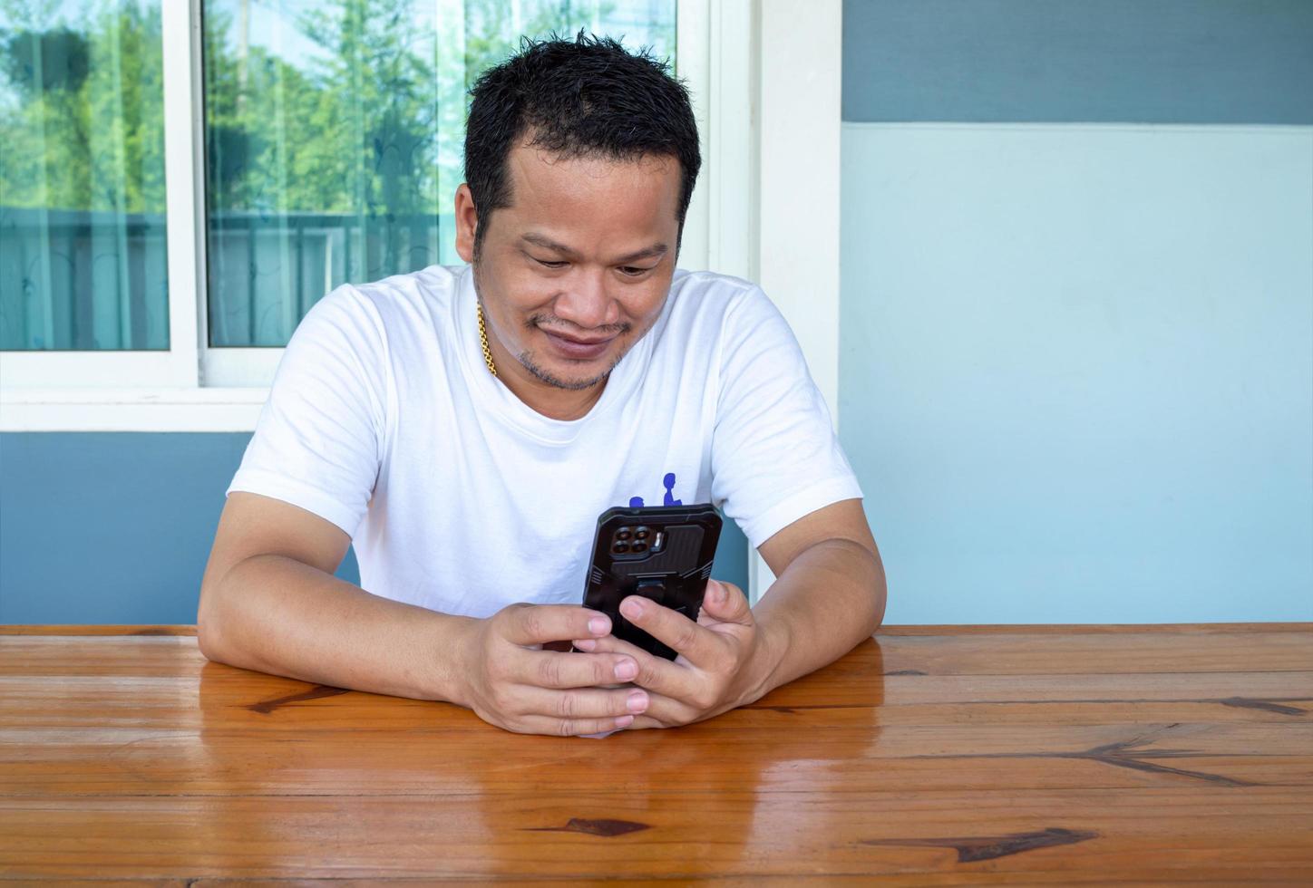 asiatisk man som bär vit skjorta med telefonen på ett träbord foto