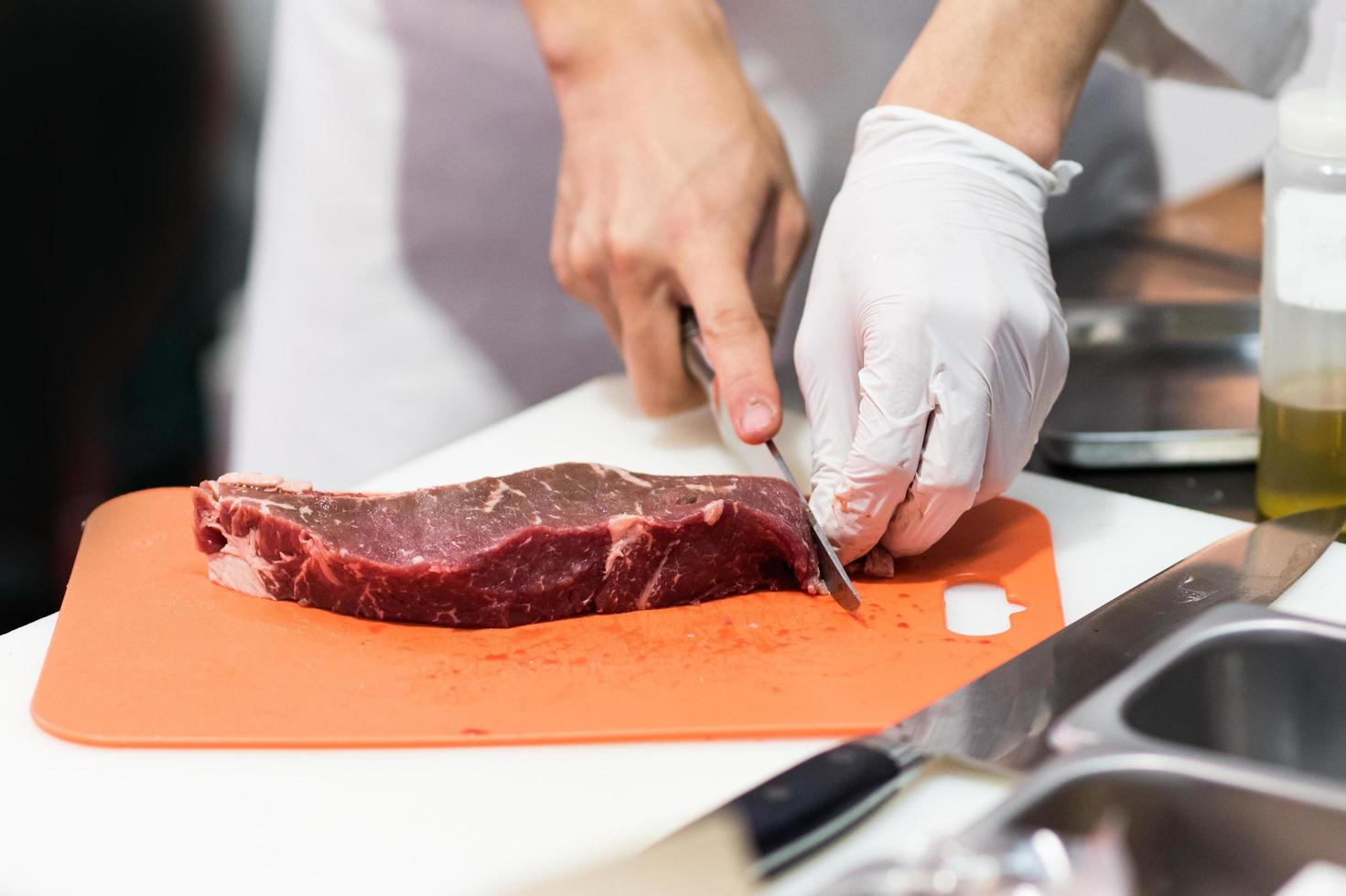 kock som skär färskt rått kött med kniv i köket foto