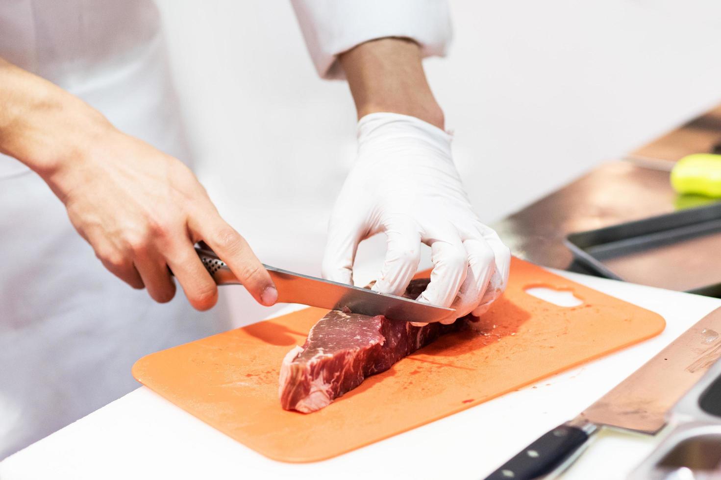kock som skär färskt rått kött med kniv i köket foto