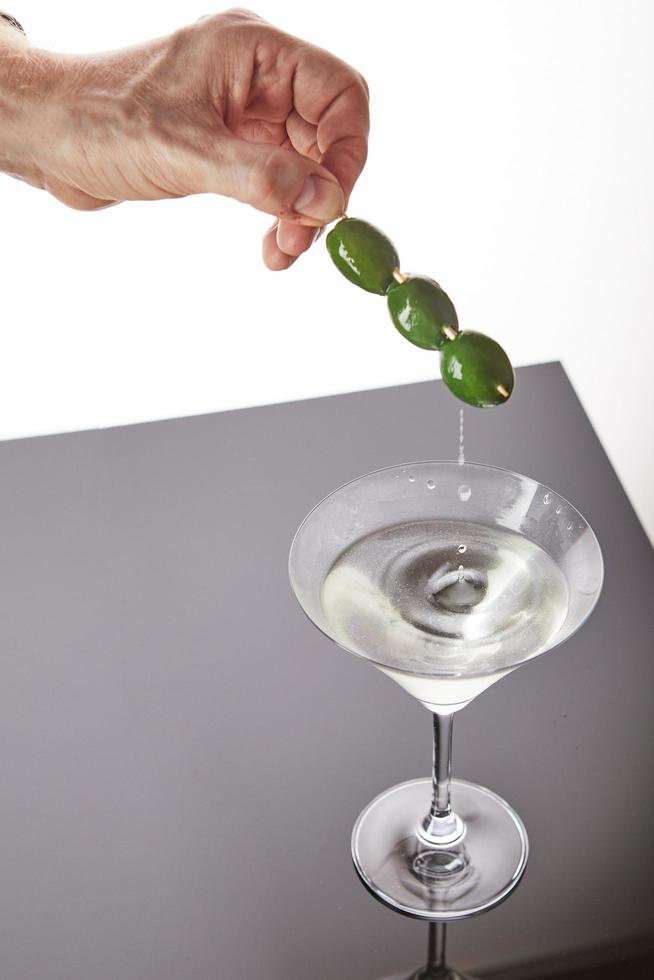 glas med martini och en hand som håller oliver på en pinne foto