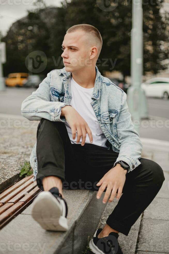 urban begrundande. ung man i denim jacka djup i trodde. stad funderar. grublande ung kille i eleganta denim jacka. omtänksam stadsbor. ung man reflekterande i hans denim jacka foto