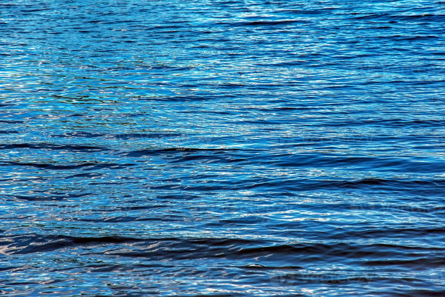 vatten krusning textur bakgrund. vågig vatten yta under solnedgång, gyllene ljus reflekterande i de vatten. foto