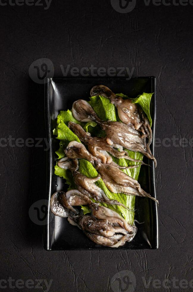 otroligt kokta bläckfiskar med grön sallad på en svart tallrik.kinesisk kök, köttgryta ingrediens foto