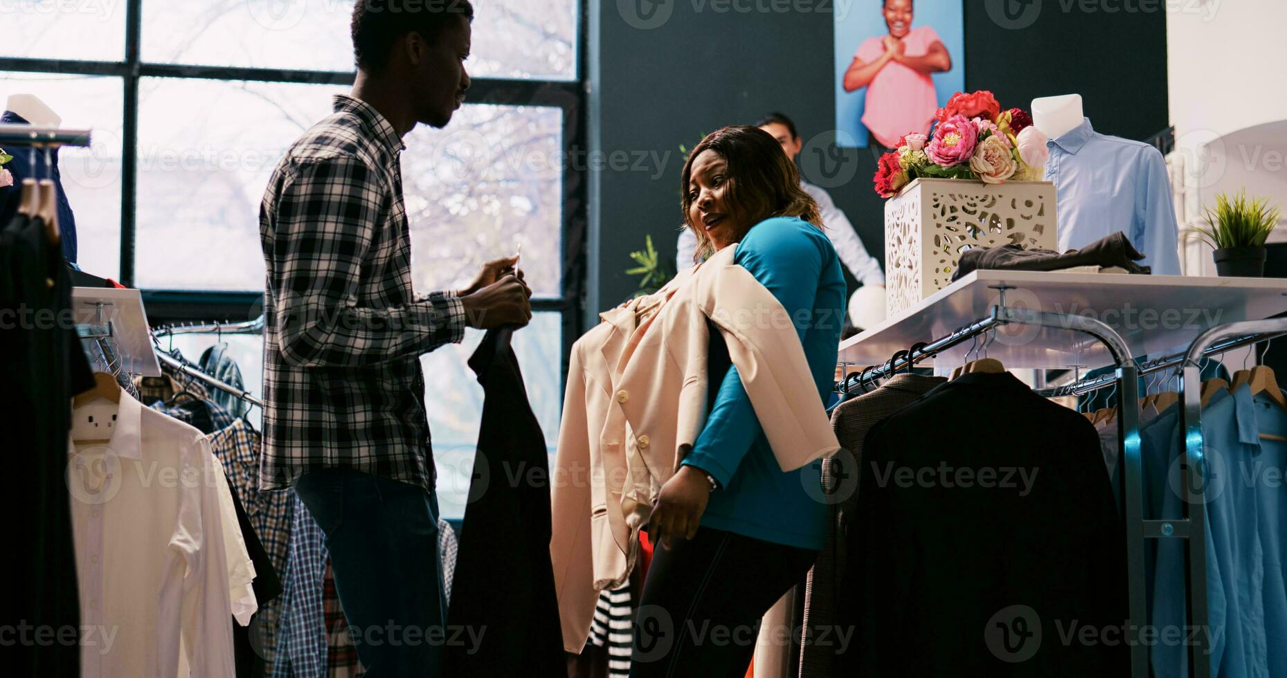 afrikansk amerikan klienter innehav eleganta kläder, spelar med med handelsvaror i Kläder Lagra. dumbom lekfull par njuter handla session, uppköp tillfällig ha på sig i modern boutique foto
