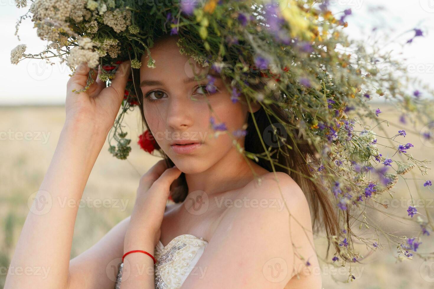 skön kvinna med en krans på henne huvud Sammanträde i en fält i blommor foto