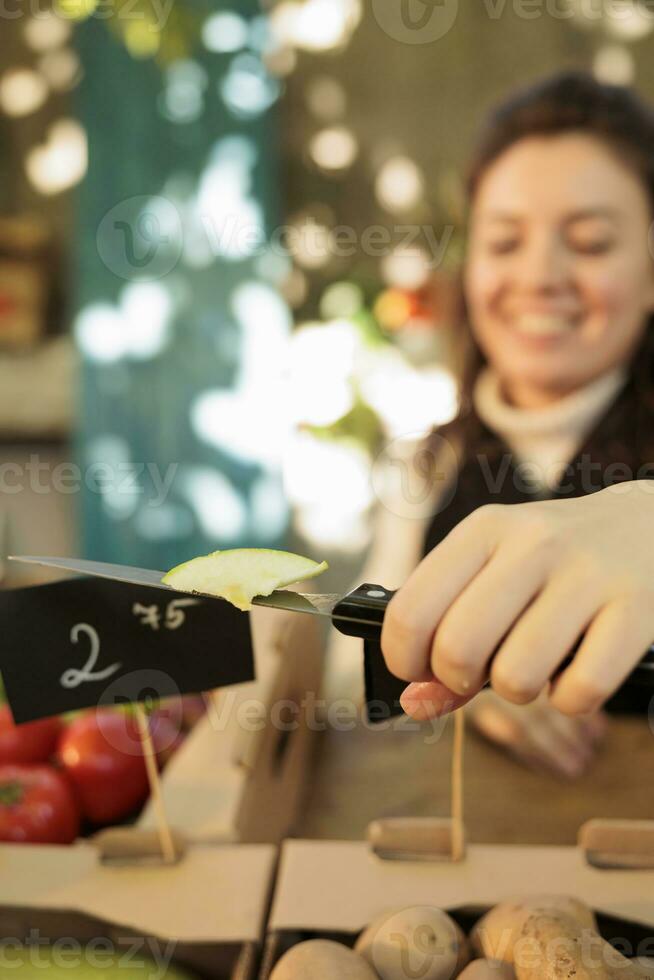 kvinna marknad Säljare ger fri frukt prover på lokal- bås, presenter färsk bio Produkter till kunder. ung jordbrukare skärande äpplen eller grönsaker organisk producera, friska mat. stänga upp. foto